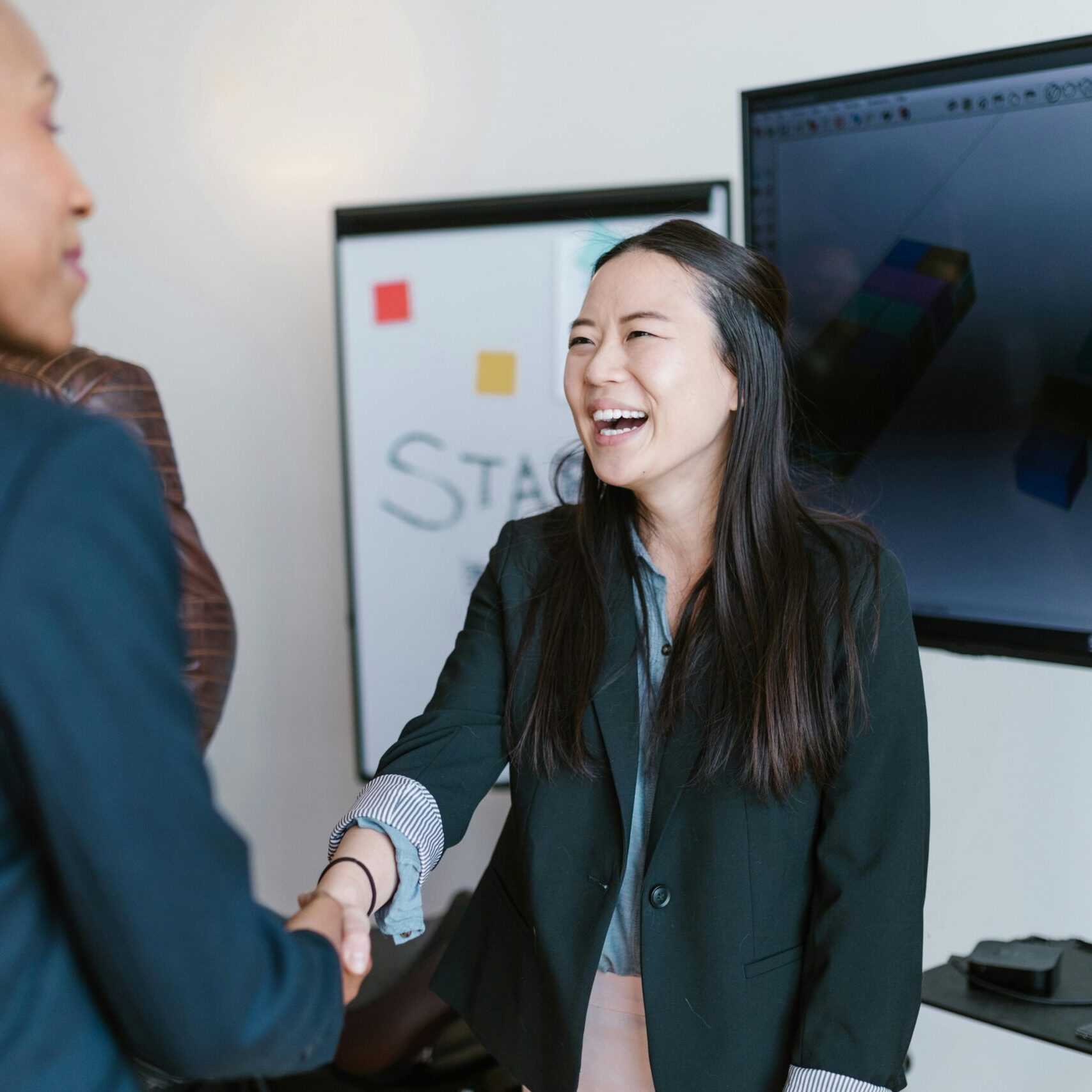 Two people smiling and shaking hands, dressed in professional attire